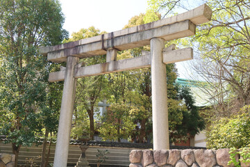 Osaka, Japan - April 14, 2024: The concrete Torii gate to Hokoku Shrine marks the entrance to Horikoshi Shrine, a centuries-old Shinto shrine, surrounded by a lush green forest of large trees.