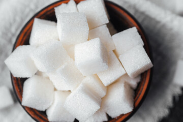 Sweet sugar cubes in a brown bowl on a textured cloth table