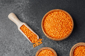 Vibrant orange lentils displayed in wooden bowls on a dark surface