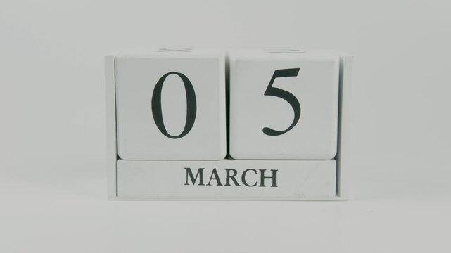 A hand flips a wooden calendar from October 5th to October 6th on a white background, marking the passing of time and the start of a new day