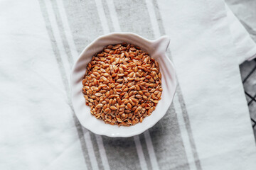 Flaxseeds in a white bowl on a linen tablecloth at home kitchen