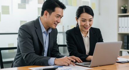 Obraz premium Two Asian Businesspeople Collaborating on Laptop