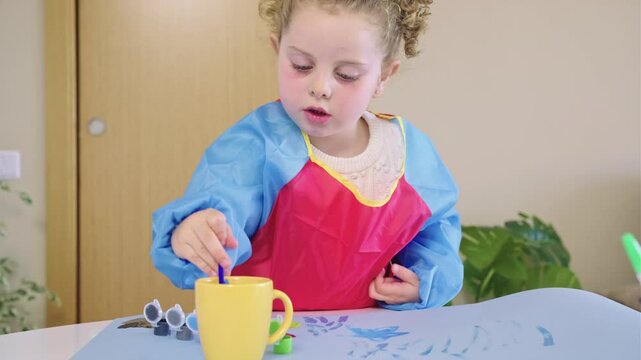 Little girl painting with tempera colors on paper sheet