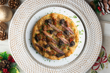 Authentic Italian focaccia with salted anchovies, sun-dried tomatoes, and black olives. Top view table with christmas decorations.