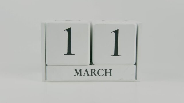 A hand flips a wooden calendar from October 11th to October 12th on a white background, marking the passing of time and the start of a new day