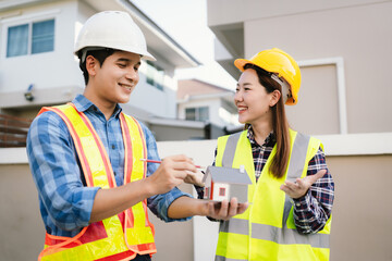 Two engineers wearing hard hats discuss blueprints and plans at an outdoor construction site, using laptops to review architecture.