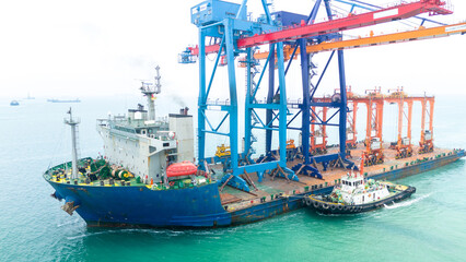 Aerial view of a heavy lift vessel transporting massive port cranes across turquoise waters. Concept of industrial shipping, maritime logistics, port construction, and oversized cargo transportation.