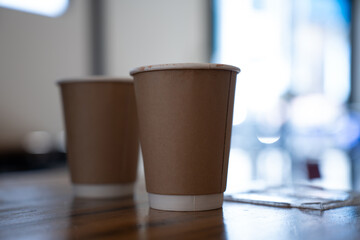 Two takeaway coffee cups on a wooden table in a cozy café setting. Warm atmosphere with natural light and soft focus background. Concept of casual conversation, coffee break, or cafe lifestyle.