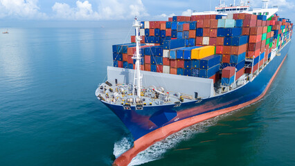 Aerial front view of a large cargo ship fully loaded with colorful shipping containers navigating...