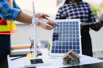Architects and engineers collaborate at a desk with blueprints and solar panels, planning...