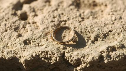 A delicate rose gold ring rests on a rough stone surface, illuminated by soft light creating subtle shadows. 