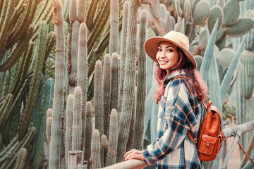 Young woman with backpack and hat enjoying a sunny day visiting a desert botanical garden,...