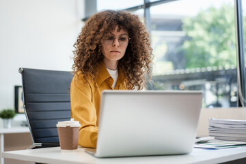 Confident Russian businesswoman sits indoors at her desk, dressed in formal attire,  paperwork and planning. Stylish and efficient, she manages tasks, notes ideas, and leads with professionalism.