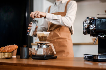 A young woman with curly hair and a headband, wearing a brown apron, prepares pour-over coffee on a wooden countertop in a bright kitchen. Focused and calm, she enjoys her morning routine.