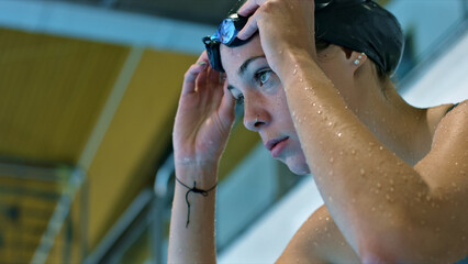 Athletic swimmer in goggles and cap adjusts fit, highlighting dedication and focus in indoor pool training.