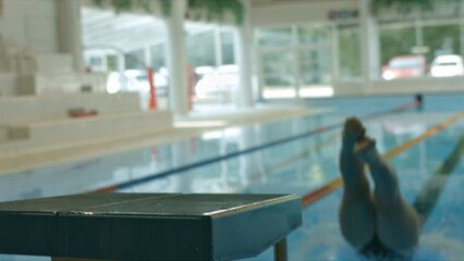 A swimmer's feet dive into a pool, highlighting the intensity and focus of indoor swimming...