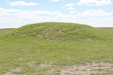 Obraz premium A grassy mound rises against a blue sky with white clouds
