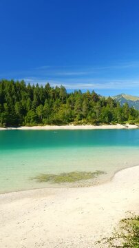 Still turquoise lake surrounded by lush alpine hills and forest in Tirol, serene Urisee nature view under clear blue sky