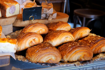 Golden brown croissants on a silver tray in a bakery setting, showcasing flaky layers and a glossy surface under warm lighting.