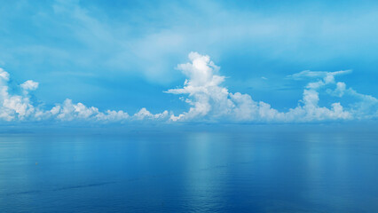 Obraz premium Scenic aerial view of a peaceful seascape with a long pier extending into calm blue waters, surrounded by ships and distant skyline under a vast cloudy sky. Maritime and coastal development concept.