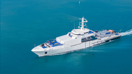 Aerial view of a modern patrol vessel sailing on calm turquoise sea, equipped with radar, deck equipment, and a helipad. Concept of maritime security, naval operations, and coast guard missions.