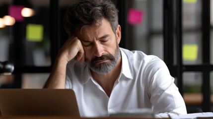 Obraz premium Thoughtful man with beard resting his head on hand at a desk