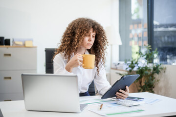 Confident Russian consultant sits at modern desk, analyzing market data on laptop. reports and...