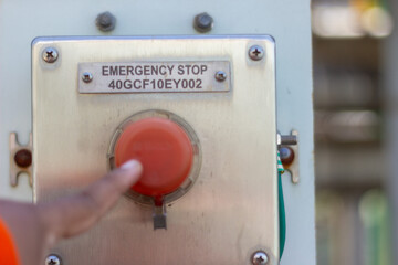 Hand pressing industrial emergency stop button. Red safety control for immediate halt in factory/plant