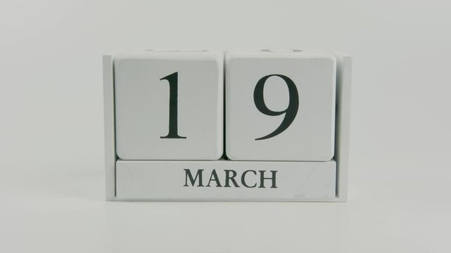 A hand flips a wooden calendar from October 19th to October 20th on a white background, marking the passing of time and the start of a new day