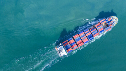 Aerial top view of a large cargo ship fully loaded with colorful shipping containers navigating...