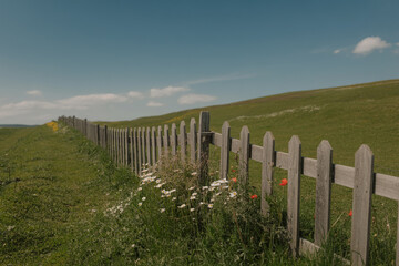 Obraz premium Rustic Wooden Fence Bordering A Green Grassy Hillside Under A Sunny Blue Sky