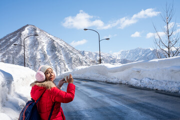 A person in red winter clothes walks along a snow-covered mountain road under a clear blue sky....