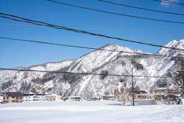 Snow-covered village nestled at the base of majestic winter mountains under a clear blue sky. Power...