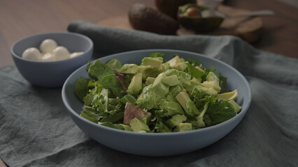 Man making salad with mixed greens avocado and mozzarella in blue bowl