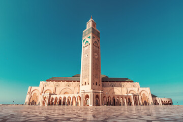 Hassan II Mosque under blue sky with ornate details and geometric patterns on the paved square