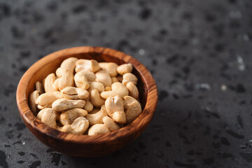 Dry cashew nuts in wood olive bowl on concrete background with copy space
