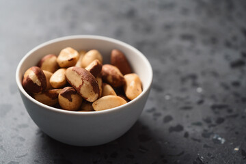 Brazil nuts in white bowl on concrete background with copy space