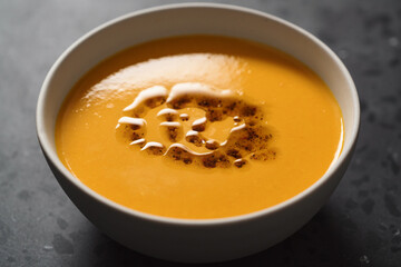 Pumpkin soup decorated with herbs and olive oil in white bowl on concrete background