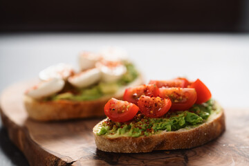 Bruschettas with avocado, tomato and mozzarella on wood board on concrete bacground