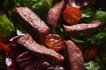 Steak salad with cherry tomatoes and mixed greens in black bowl