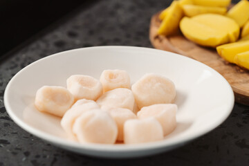 closeup of frozen scallops in white bowl on walnut table for defrosting