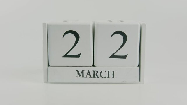 A hand flips a wooden calendar from October 22nd to October 23rd on a white background, marking the passing of time and the start of a new day
