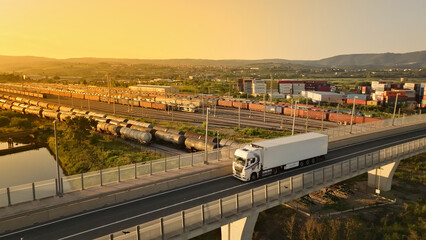 Aerial view of a truck driving on a bridge, surrounded by train tracks and cargo containers,...