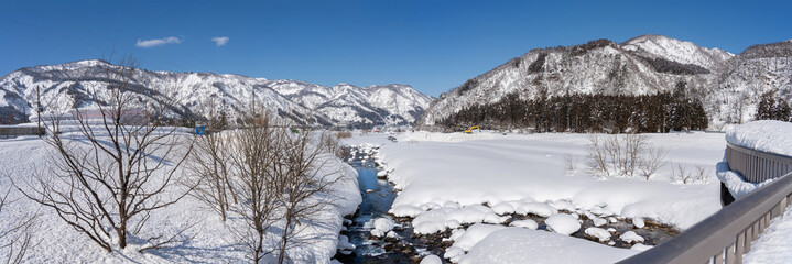 Snow-covered mountains under a clear blue sky create a breathtaking winter scene. The untouched snowy foreground enhances the majestic beauty of the rugged peaks in serene, crisp air.