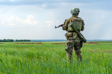 Ukrainian soldier is standing vigilantly in an open field, prepared for any potential threat that...
