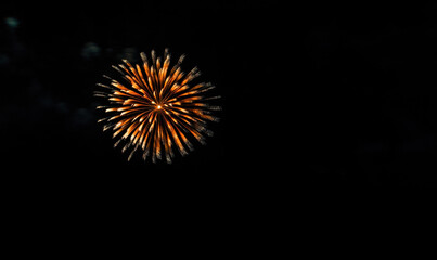 Obraz premium A single, vibrant orange firework explodes against a deep black night sky, creating a stunning circular burst of light and color. : Generative AI