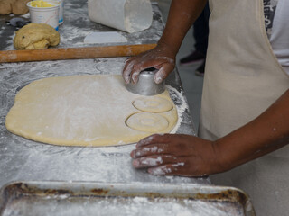 Close-up of hands skillfully using a cutter to shape doughnut dough on a floured surface
