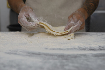 Close-up shot of hands expertly layering thin dough sheets on a floured surface