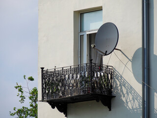 Elegant Black Wrought Iron Balcony with Satellite Dish on Light Plaster Building Facade in Urban...