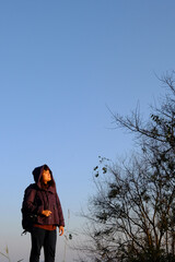 Traveler Asian woman wearing jacket and hood standing on green lawn grass and blue sky with sunrise...